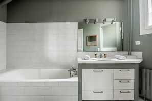 A modern bathroom with a white bathtub, a sink with a mirror above it, and a vanity with drawers. - Mellow Grace, by Veeve (Paris)