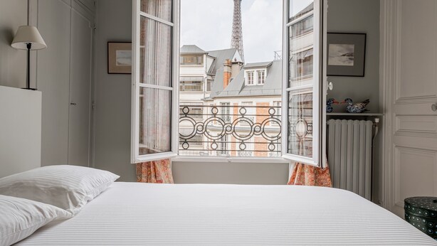 A bedroom with a view of the Eiffel Tower through an open window with a decorative iron grille. - Mellow Grace, by Veeve (Paris)