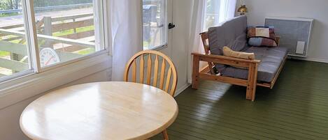 A room with a round wooden table and two chairs, a sofa, and a radiator.