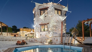 Ein Poolbereich mit einem Steinhaus, einer Holzterrasse und einer Pergola.