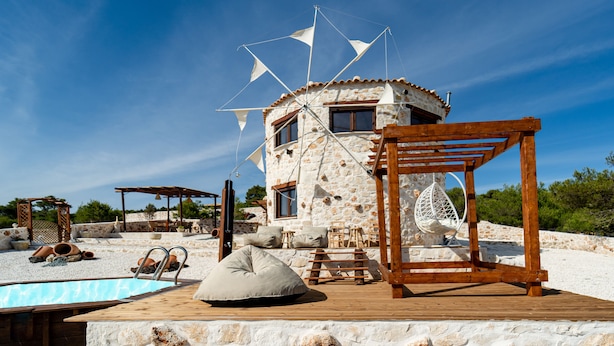 Ein Steinhaus mit einer Holzterrasse, einem Hängestuhl und einem Pool.