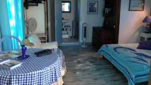 Une pièce avec une table à carreaux, un lit à motifs bleus et blancs, une chaise, une commode et un ventilateur.