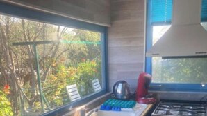 Une cuisine compacte dotée d’un plan de travail en bois, d’un évier, d’une cuisinière à gaz et d’une fenêtre donnant sur un espace verdoyant.