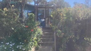 Un escalier en pierre mène à un espace abrité agrémenté d’une pergola, le tout entouré de plantes et d’arbres en fleurs.