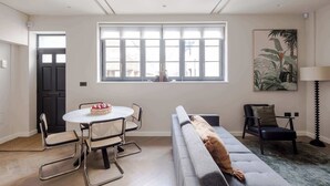 A modern living room with a round dining table, two sofas, and a large window with blinds. - Marylebone Mews House · Regent's Park · Sleeps 6 (London)
