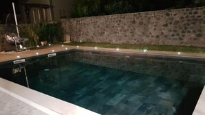 Ein rechteckiger Swimmingpool mit Steinmauer und Fliesenveranda.