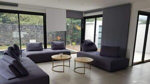 Ein modernes Wohnzimmer mit zwei Sofas und zwei runden Couchtischen, großen Schiebeglastüren und einer dahinter sichtbaren Steinwand.