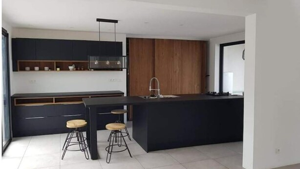 Eine moderne Küche mit dunklen Schränken, einer zentralen Kochinsel mit Hockern und einer Wand mit Holzverkleidung.