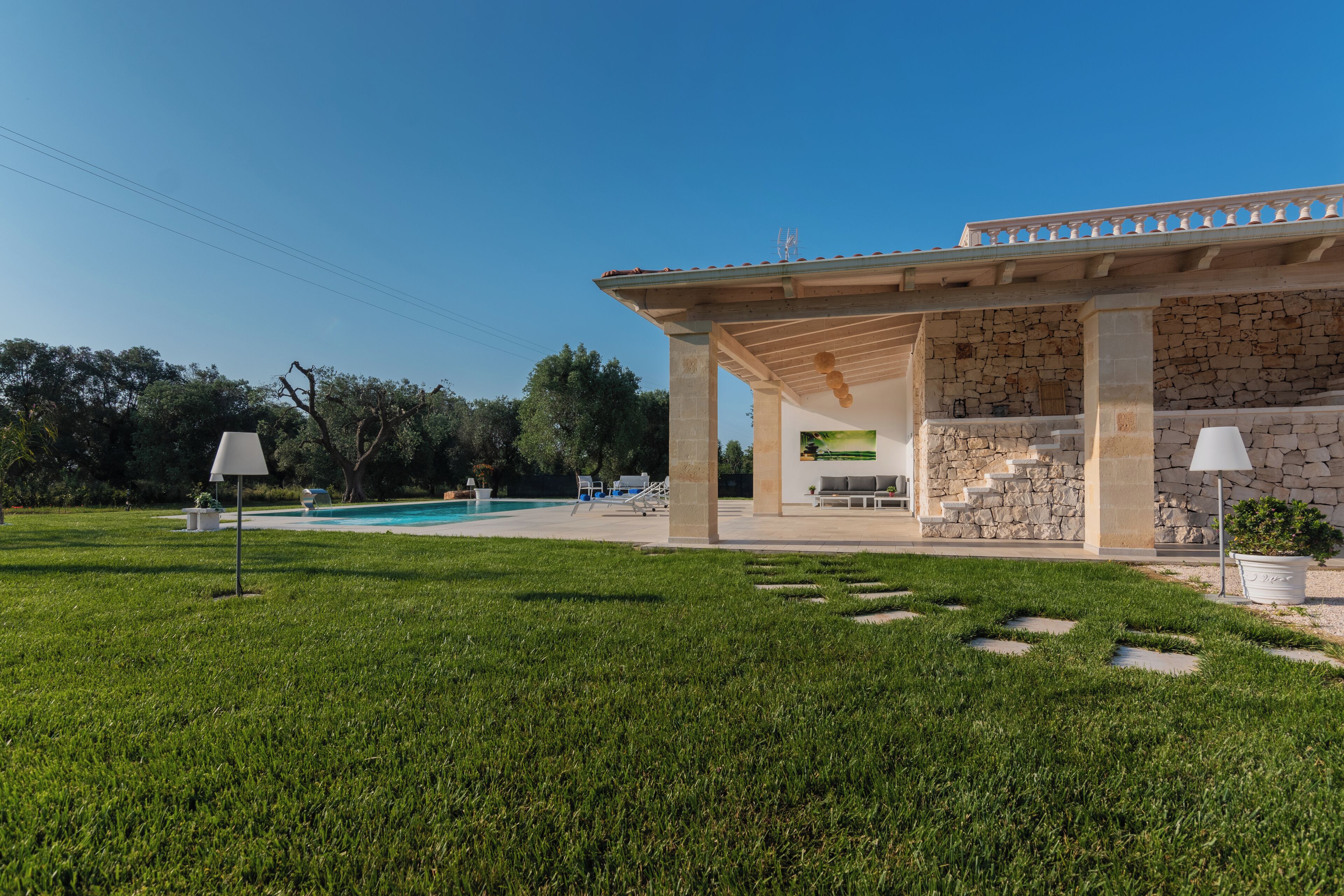 Un espace aménagé au bord de la piscine, avec une structure en pierre, des sièges d’extérieur et un ciel d’un bleu limpide.