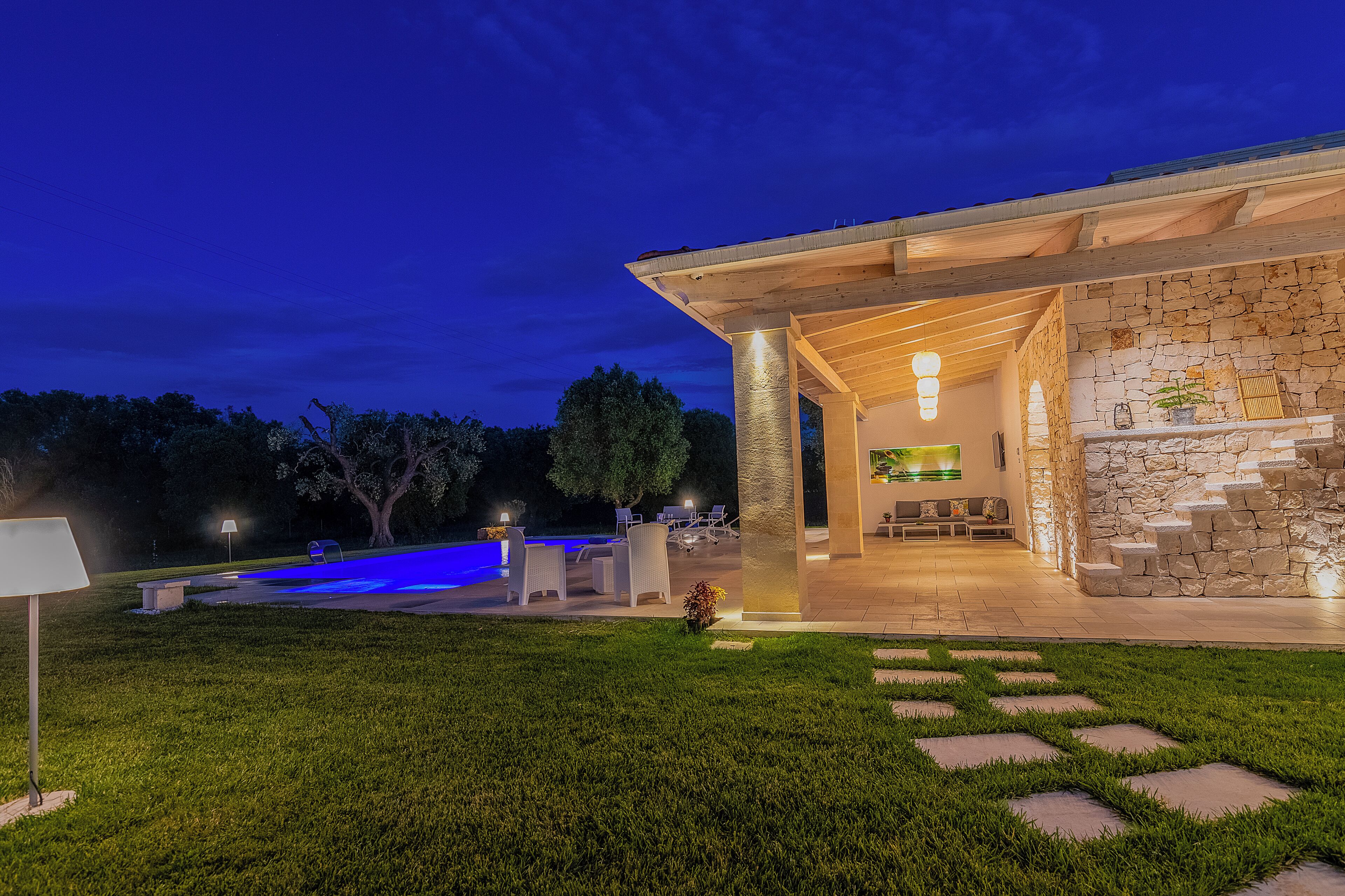 Un patio exterior moderno con muros de piedra, una piscina y mobiliario de exterior.