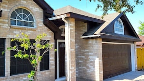 Ein zweistöckiges Haus mit Ziegelverkleidung, eine Garage mit brauner Tür und ein Baum davor.