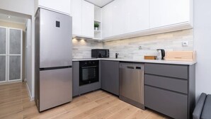 A modern kitchen with stainless steel appliances, grey cabinetry, and a wooden floor.