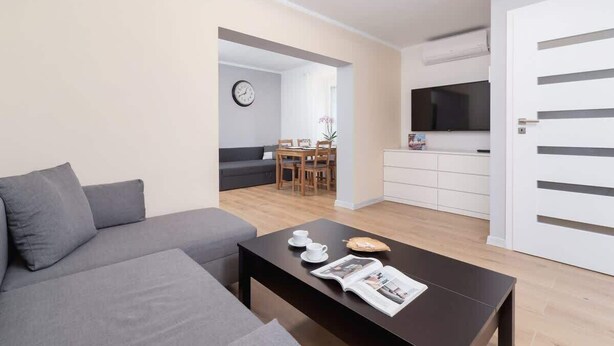 A modern living room with a grey sofa, a coffee table with a magazine, and a dining area with a table and chairs.