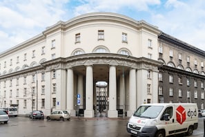A large, classical building with a central entrance flanked by columns, a parking sign, and a white van with a red logo.