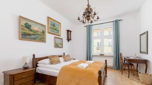 Ein Schlafzimmer mit einem hölzernen Bett, einem Nachttisch, einem Schreibtisch und einem Fenster mit Vorhängen.