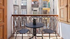 Ein Balkon mit rundem Tisch und zwei Stühlen, einem Metallgeländer sowie Blick auf ein Wohngebäude mit Balkonen und Fenstern.