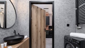 A modern bathroom with a wooden door, a round mirror, a black sink, and a black washing machine. - Stylish Apartment | Air Conditioning and Patio with Garden (Kraków)