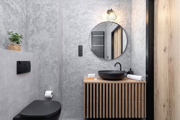 Un baño moderno con un espejo redondo, lavamanos negro, tocador de madera y un inodoro negro.