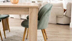 Una sala de estar moderna con una mesa de comedor de madera, sillas tapizadas en verde, un sofá beige y un televisor de pantalla plana en la pared.