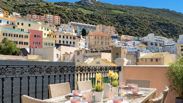 Un comedor con mobiliario de mimbre y una mesa dispuesta para cuatro, con vistas a un pueblo en la ladera y edificios.