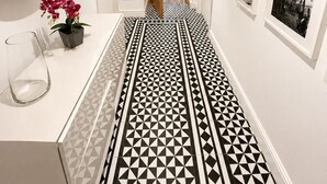 A hallway with a geometric patterned floor, a mirror, a potted plant, and framed pictures on the walls. - Grand Central House - Penthouse Double Room (Gibraltar)