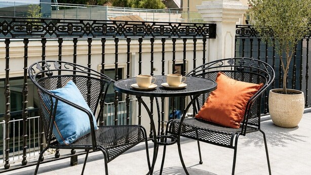 A balcony with two chairs and a table, overlooking a cityscape with colorful buildings and a hill. - City Penthouse Suite w/ Terrace (Gibraltar)