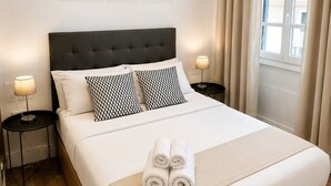 A neatly made bed with a headboard, two bedside tables with lamps, and three framed pictures on the wall. - Grand Central House - Classic One Bedroom Balcony (Gibraltar)