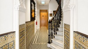 A hallway with ornate white arches, a patterned tiled floor, and a staircase with black railings. - Grand Central House - Classic One Bedroom Balcony (Gibraltar)