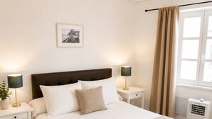 Une chambre d’hôtel bien rangée, avec un lit, des tables de chevet, une lampe, un tableau au mur et une fenêtre avec des rideaux.