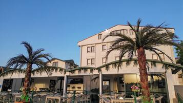 Un hotel con fachada blanca, varios balcones y zonas de estar al aire libre con sillas y mesas.