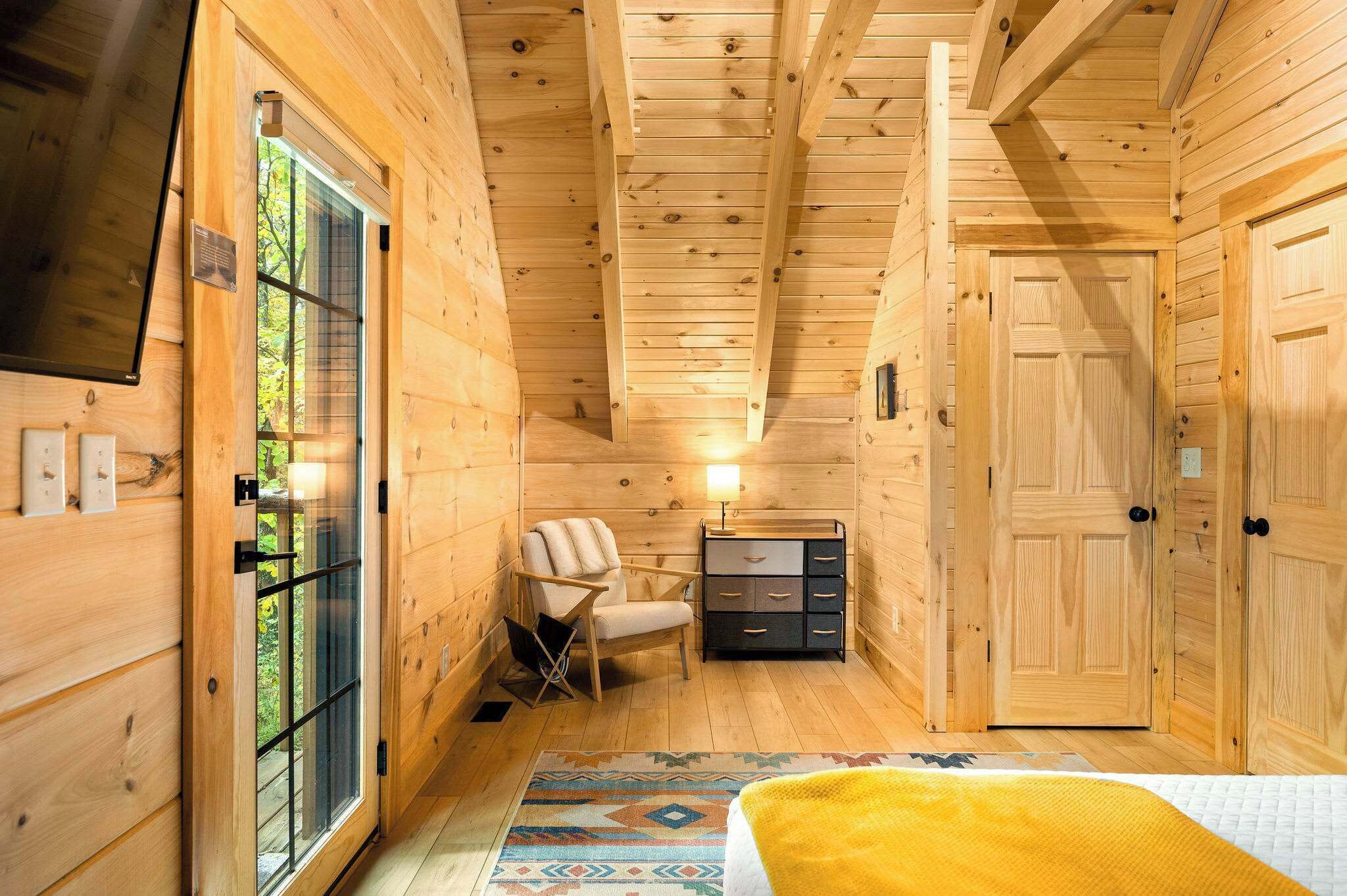 Quarto de cabana de madeira com cama, cadeira, cômoda e porta.