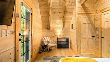 Quarto de cabana de madeira com cama, cadeira, cômoda e porta.