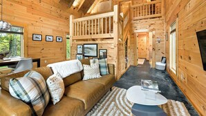 Ein Holzblock-Innenraum mit Schlafzimmer auf Schlafhöhe, einer Couch, einem Esstisch und gerahmten Bildern an den Wänden.