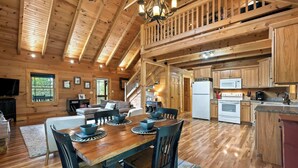 Una cabaña de madera espaciosa con comedor, cocina y una escalera que sube a un altillo.