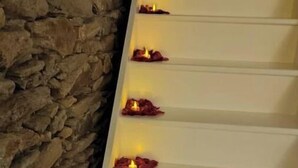 Una escalera adornada con velas y pétalos de rosa en cada peldaño, que conduce a un muro de piedra.