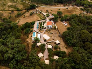 Vista aérea de uma propriedade com piscina, vários edifícios e vegetação ao redor.
