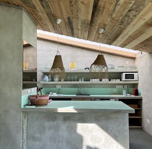 Cozinha com bancada verde, luminárias trançadas penduradas e um micro-ondas.