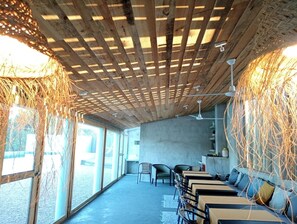 Um interior moderno com teto de madeira, janelas amplas e área de estar com mesas e cadeiras.