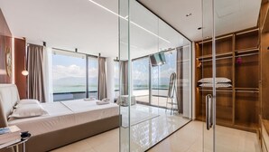 Une chambre d’hôtel moderne équipée d’un lit, d’un bureau, d’une chaise, d’une cloison en verre et offrant une vue sur la mer.