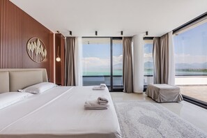 A modern hotel room with a large bed, a small table, and a view of the sea.