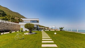 Un bâtiment moderne doté d’un mur en pierre, d’une pelouse verdoyante, d’une clôture blanche et offrant une vue dégagée sur la mer.