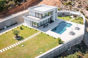 Una casa moderna de dos pisos amb piscina, un mur de pedra de sostén i un jardí ben cuidat.