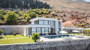 Une maison moderne à deux étages, avec un mur de pierre en premier plan, une piscine et une vue sur un paysage montagneux.