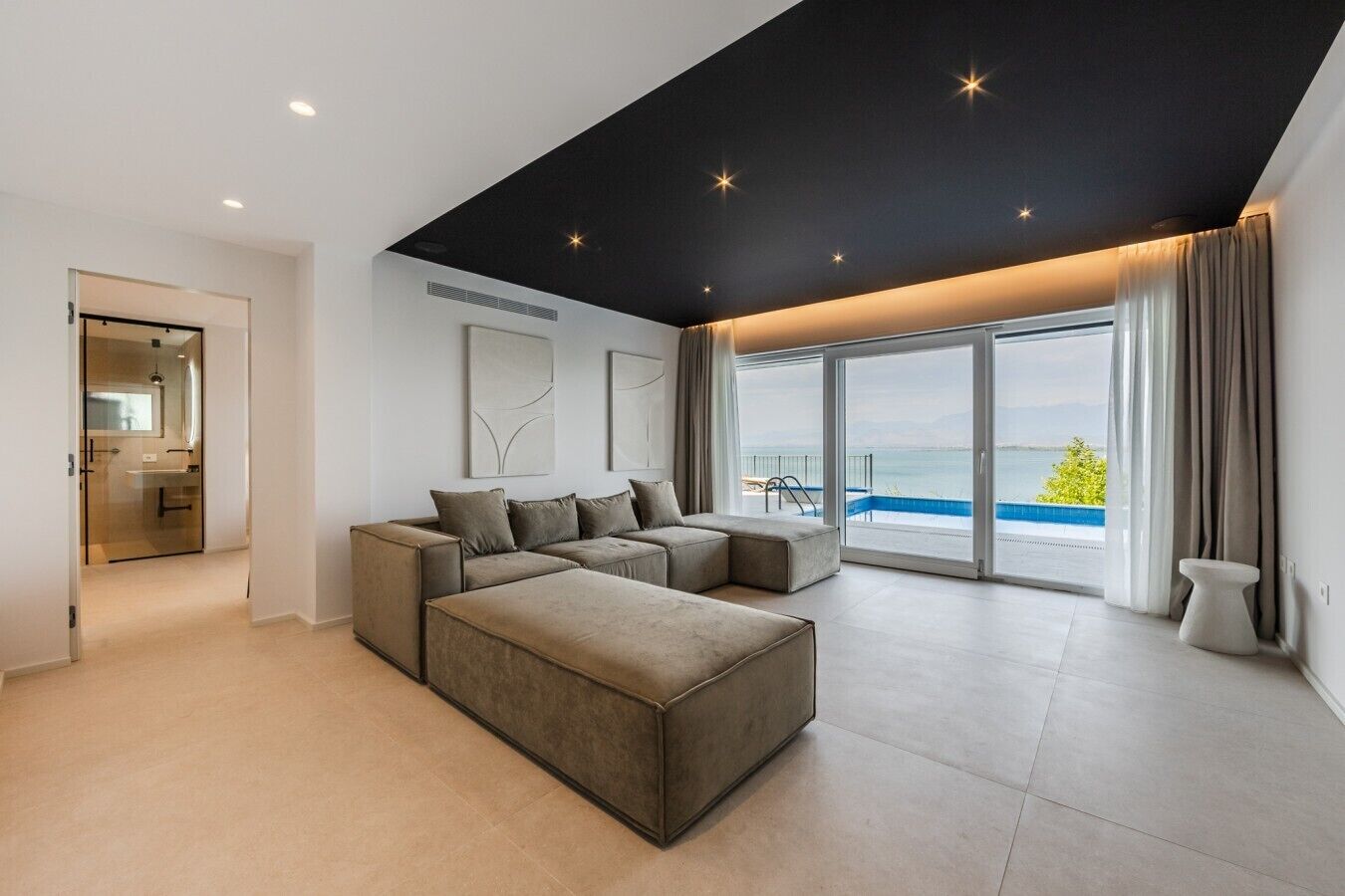Un salon moderne avec un canapé d’angle et une grande fenêtre donnant sur une piscine.