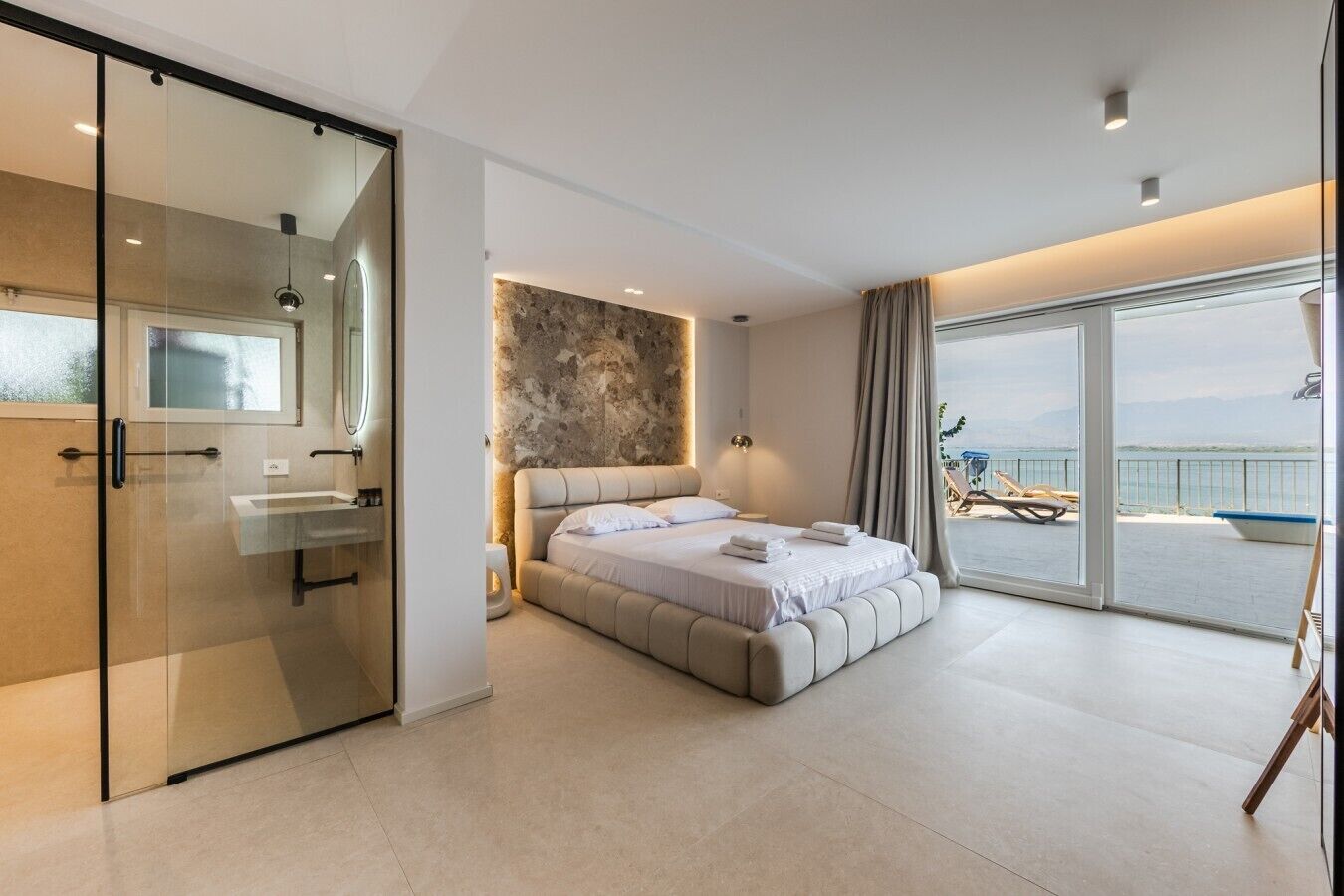 Ein modernes Schlafzimmer mit einem großen Bett, einer Duschkabine aus Glas und einem Balkon mit Aussicht.