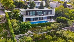 Ein modernes, zweistöckiges Haus mit Swimmingpool, umgeben von üppiger Bepflanzung und weiteren Wohngebäuden.