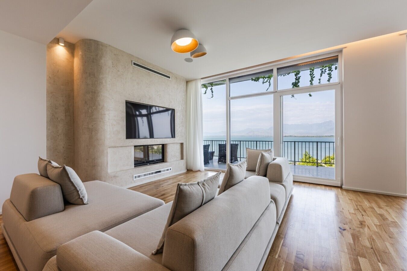 Ein modernes Wohnzimmer mit Flachbildfernseher, Kamin und großem Fenster mit Blick auf einen See und Berge.