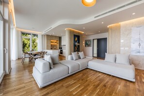Un salon moderne doté d’un grand canapé d’angle, d’un coin repas avec une table et des chaises, et d’une cuisine en arrière-plan.