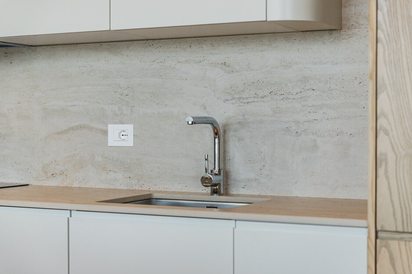 A kitchen with a single stainless steel sink, a light-colored countertop, and a concrete backsplash.