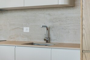 A kitchen with a single stainless steel sink, a light-colored countertop, and a concrete backsplash. - Sunset | The Twin Villa by PikHost (Shiroka)